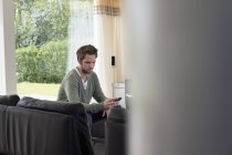 Мужчина держит мобильный телефон на диване в гостиной — стоковое фото