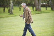 Homem elegante usando telefone celular enquanto caminha no parque — Fotografia de Stock