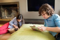 Boy and a girl using electronic gadgets at home — Stock Photo