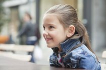 Gros plan de la petite fille souriante assise au café sur le trottoir — Photo de stock