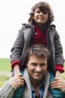 Man carrying smiling son on shoulders outdoors — Stock Photo
