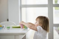 Menina bonito pegar brinquedo chá definido a partir de mesa de jantar — Fotografia de Stock