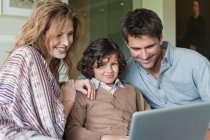 Мальчик использует ноутбук с родителями дома — стоковое фото