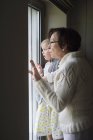 Frau mit kleiner Enkelin schaut durchs Fenster — Stockfoto