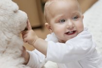Cheerful baby girl playing with soft toy and looking away — Stock Photo