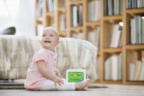 Bambina che gioca con il blocco musicale giocattolo sul pavimento a casa — Foto stock
