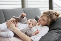 Rilassato giovane donna che riposa sul divano con figlia bambino — Foto stock