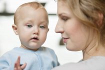 Close-up of woman looking at cute baby girl with blue eyes — Stock Photo