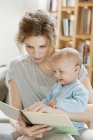 Donna insegnare bambino figlia con libro illustrativo — Foto stock
