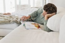 Uomo sdraiato sul letto e rivista di lettura — Foto stock