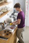 Молодой человек моет посуду на кухне — стоковое фото