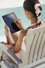 Mulher sentada em cadeira de adirondack e usando tablet digital na praia — Fotografia de Stock