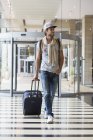 Jovem sorrindo homem puxando bagagem no aeroporto — Fotografia de Stock