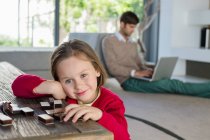 Porträt eines lächelnden Mädchens mit ihrem Vater mit einem Laptop im Hintergrund — Stockfoto