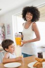 Donna e suo figlio a un tavolo da pranzo con succo d'arancia — Foto stock