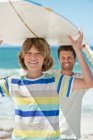 Mann und Sohn tragen Surfbrett am Strand — Stockfoto