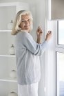 Старші жінки налаштування Вікна завісити вдома і дивлячись на камеру — стокове фото