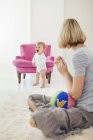 Woman looking at crying baby while sitting on white furry carpet — Stock Photo