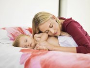 Женщина отдыхает головой на плече ребенка спит на кровати — стоковое фото