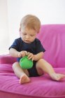 Baby boy playing with pouch bag in pink armchair — Stock Photo