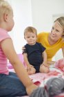 Smiling woman playing with children on bed — Stock Photo