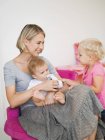 Усміхаючись молода мати сидить з дітьми вдома — стокове фото