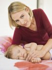 Portrait of woman reclining next to baby sleeping on bed — Stock Photo