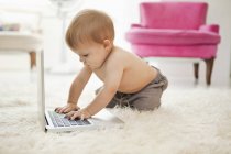 Без сорочки хлопчик грає з ноутбуком на білому пухнастому килимі — стокове фото