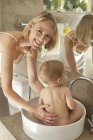 Happy woman giving bath to baby in washbasin — Stock Photo