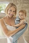 Portrait of smiling young woman holding baby in towel — Stock Photo