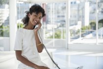 Портрет усміхненої жінки, що розмовляє по стаціонарному телефону в офісі — стокове фото