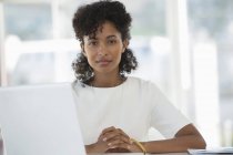 Portrait of woman sitting in front of laptop in office — Stock Photo