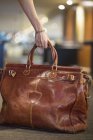 Gros plan de la main féminine ramassant sac à main en cuir de voyage — Photo de stock