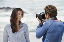 Uomo scattare foto di moglie con macchina fotografica sulla spiaggia — Foto stock