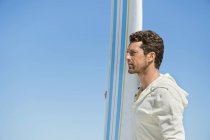 Человек держит доску для серфинга против голубого чистого неба и смотрит в сторону — стоковое фото