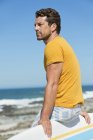 Homem sentado na prancha de surf na praia e olhando para longe — Fotografia de Stock