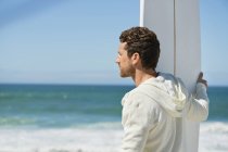 Чоловік тримає дошку для серфінгу на хвилястому морі і дивиться далеко — стокове фото