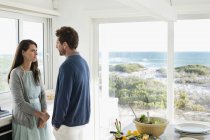 Couple talking and looking at each other in kitchen of coastal house — Stock Photo