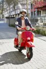 Человек в шлеме едет на красном скутере вниз по улице — стоковое фото