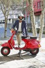 Portrait of man in helmet standing with red scooter on street — Stock Photo