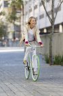 Smiling blonde woman riding bicycle on a street and smiling — Stock Photo