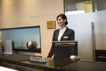 Recepcionista feminina em pé no balcão da recepção do hotel e sorrindo — Fotografia de Stock