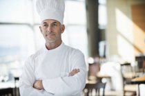 Retrato de chef varón seguro de sí mismo con los brazos cruzados en el restaurante - foto de stock