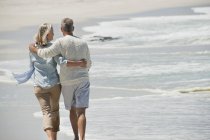 Rear view of romantic senior couple walking on beach — Stock Photo
