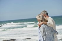 Abbracciare coppia anziana a piedi sulla spiaggia di mare — Foto stock