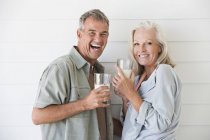 Портрет смеющейся пожилой пары, стоящей со стаканами молока — стоковое фото