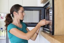Mujer poniendo comida en el horno en la cocina moderna - foto de stock