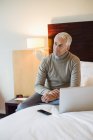 Uomo seduto con computer portatile sul letto in una camera d'albergo — Foto stock
