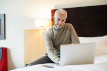 Человек с ноутбуком на кровати в гостиничном номере — стоковое фото