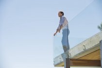 Homem pensativo em pé no terraço e olhando para o céu azul — Fotografia de Stock